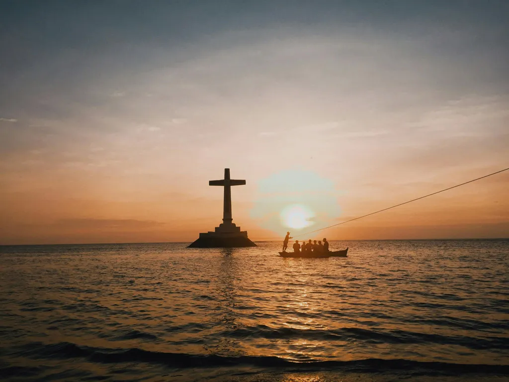 Cross at sea during sunset with boat silhouette