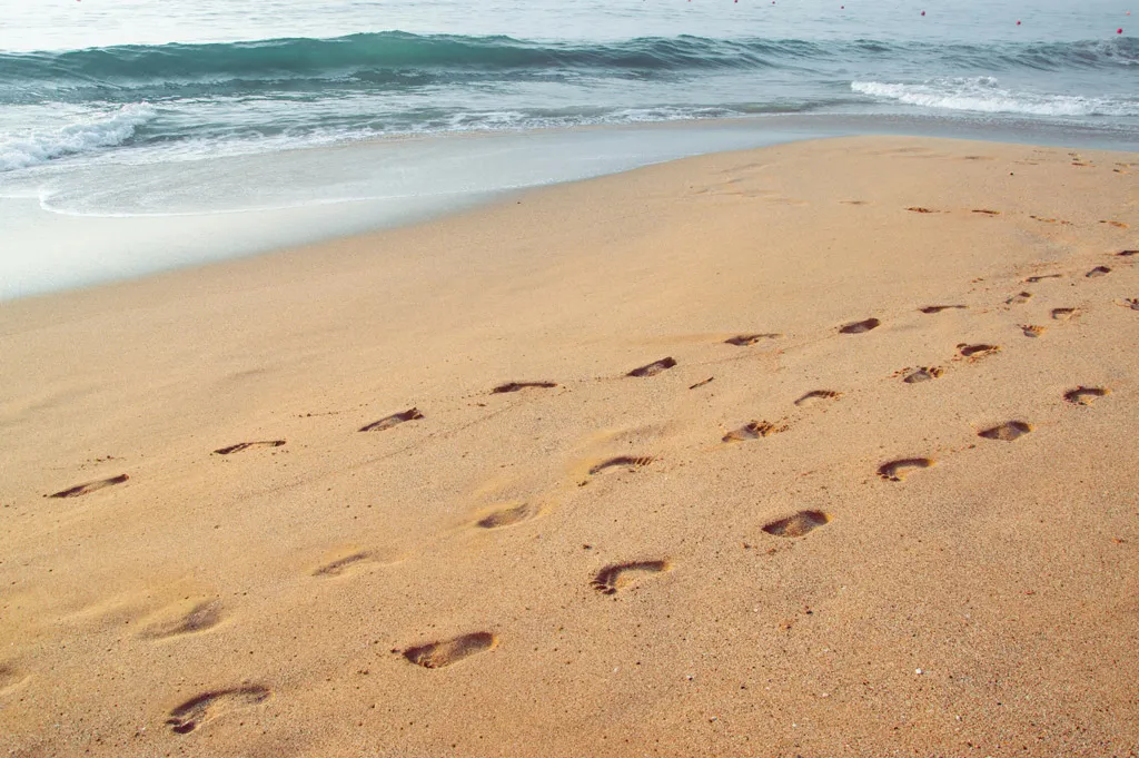 Footprints in the sand along the ocean shore, symbolizing a journey with God.