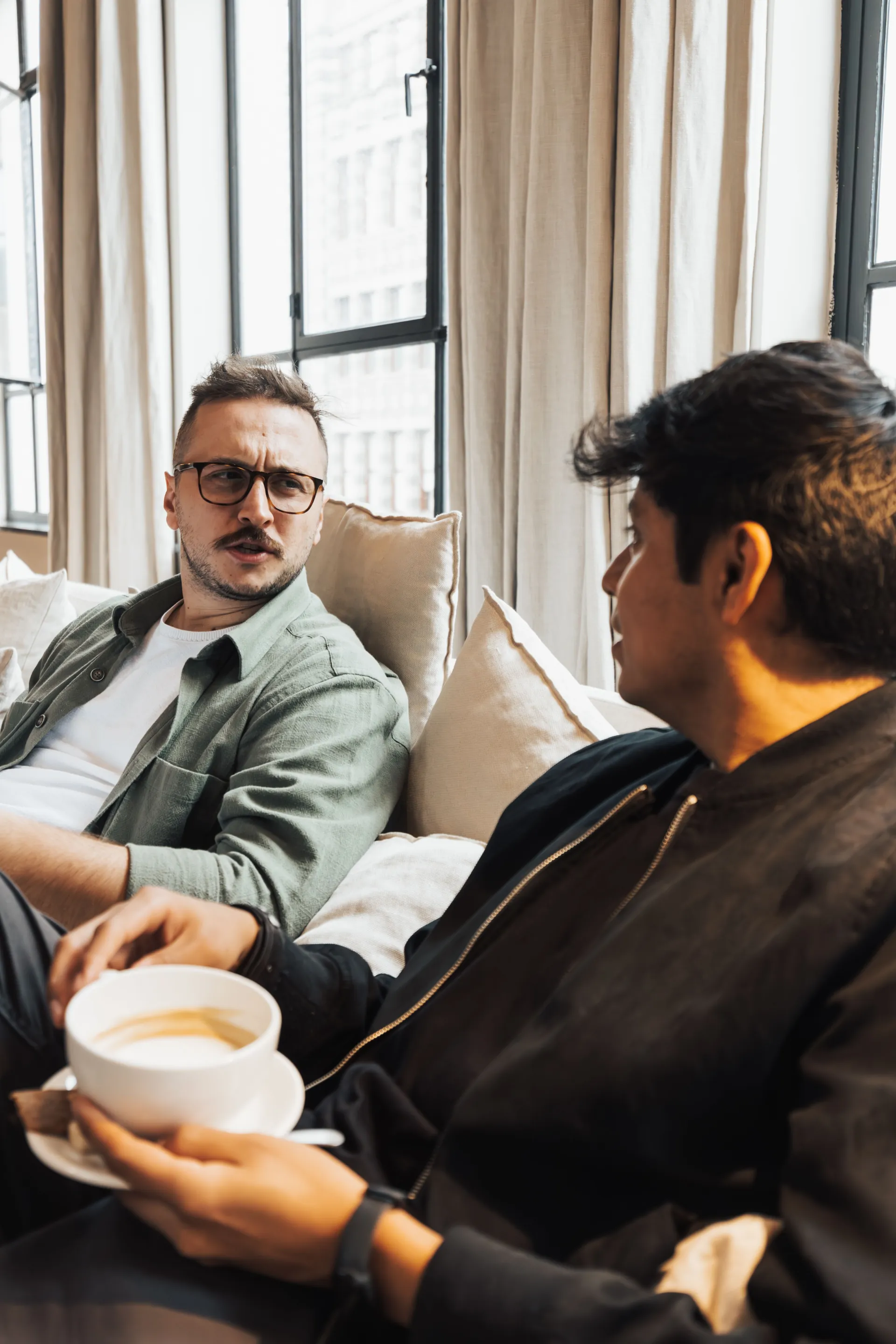 Two men sitting on a couch having an attentive and thoughtful conversation over coffee.