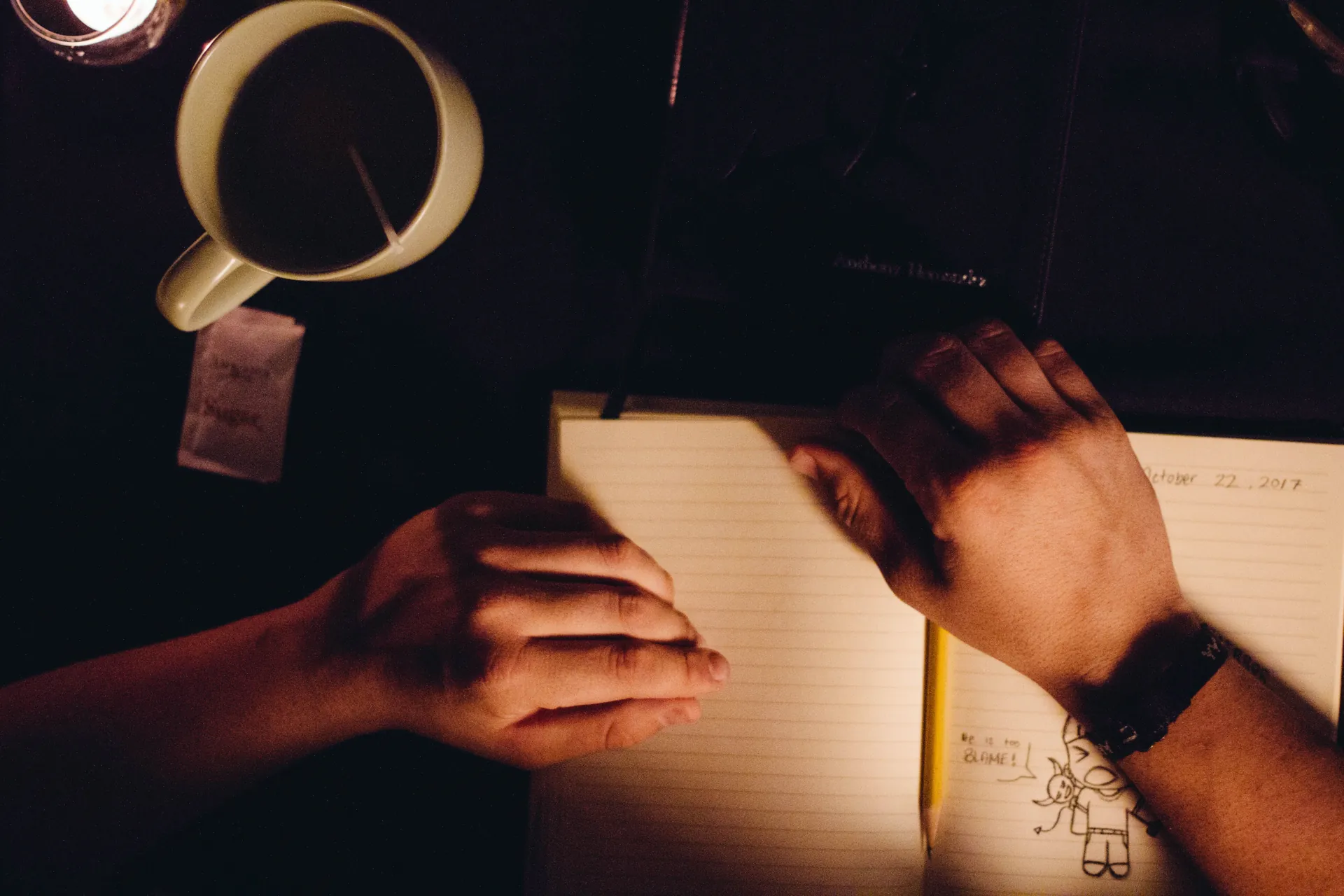 Hands resting on an open journal beside a Bible, coffee, and candlelight during a quiet devotional time.