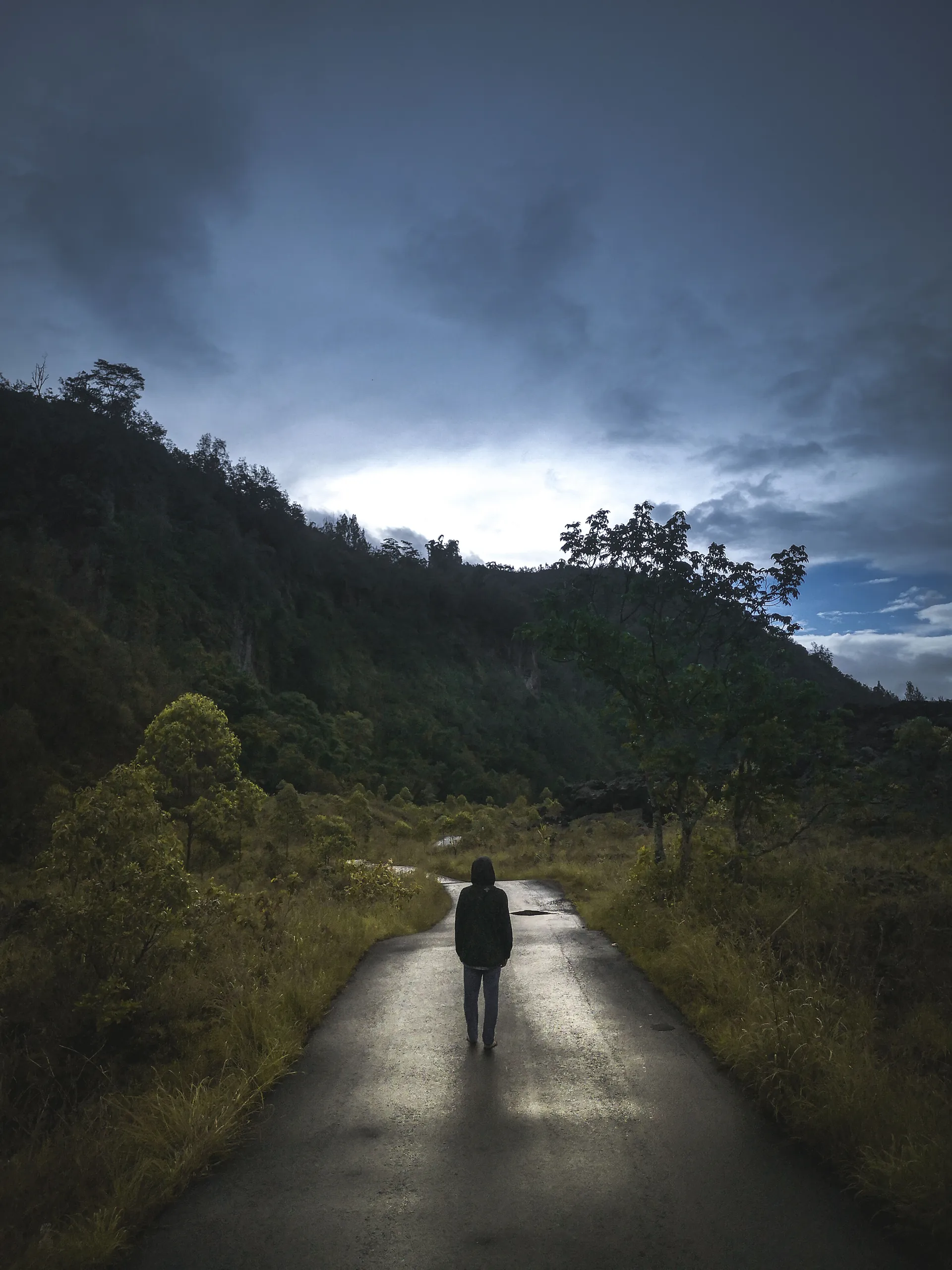 A person walking alone on a winding road beneath dark storm clouds, symbolizing perseverance and faith.
