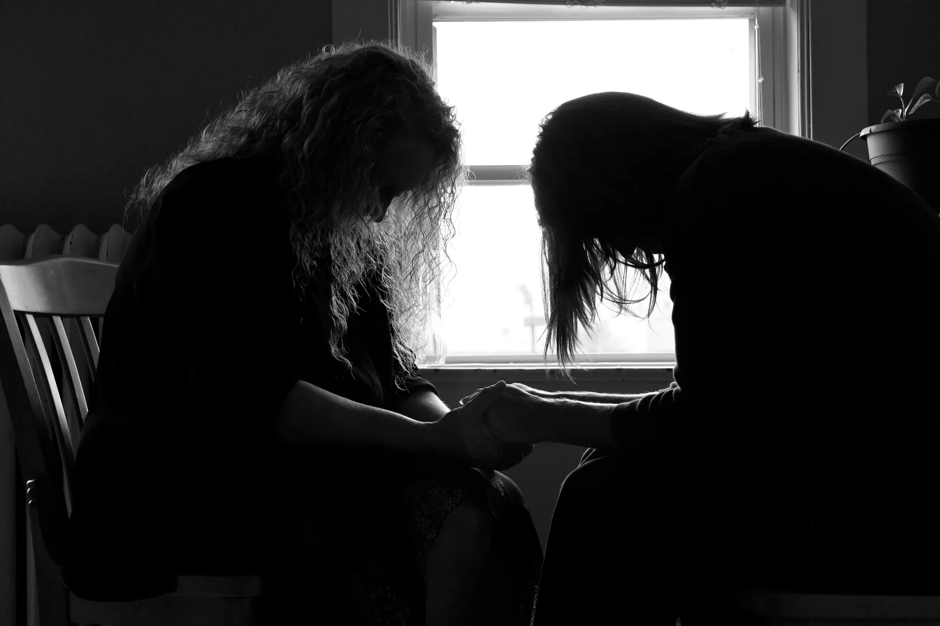 Dos personas sentadas juntas con las manos unidas en oración, apoyándose mutuamente.